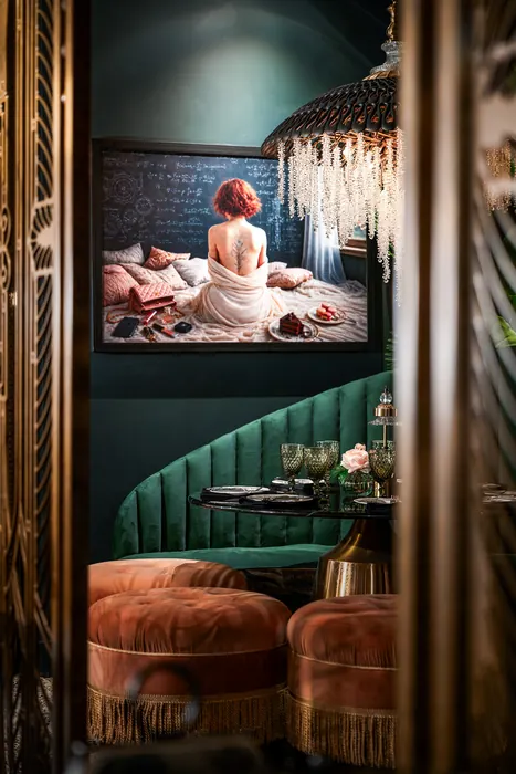 Framed artwork above an emerald velvet banquette and coral ottoman