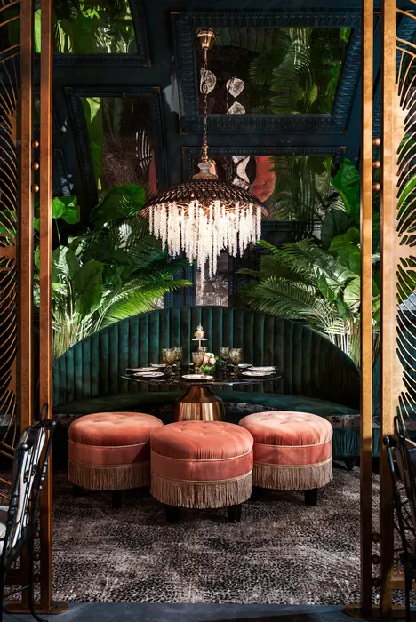 Corner banquette in emerald velvet beneath a fringed shell chandelier, framed by tropical foliage