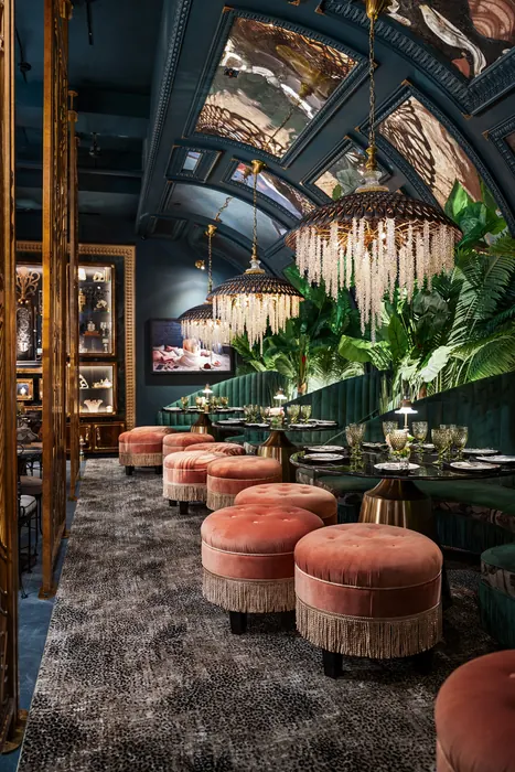 Dining tables and coral velvet ottomans under the arched mirrored ceiling