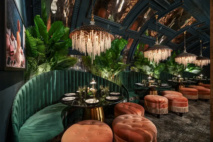 Curved emerald velvet banquette with coral tufted ottomans and brass-topped tables