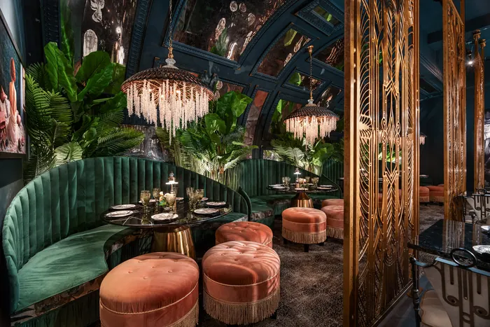 Emerald banquette seating and coral ottomans beneath hanging foliage
