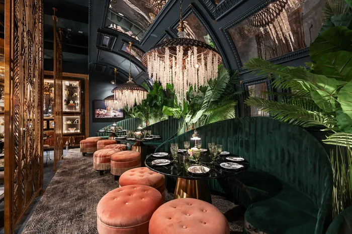 Coral tufted ottomans drawn up to a dark marble table against emerald velvet