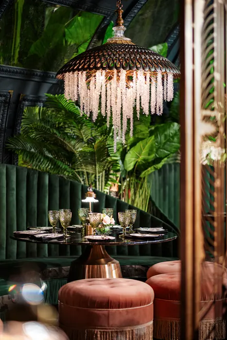 Close view of a booth set for dinner, foliage overhead and a coral ottoman alongside